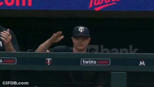 A Couple Of Baseball Players Sitting In A Dugout With A Twins Logo On The Wall GIF