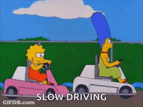 A Couple Of Cartoon Characters Are Driving Golf Carts And The Words Slow Driving Are Visible . GIF