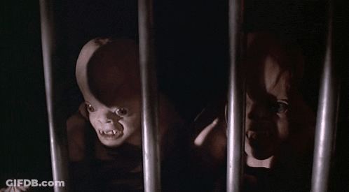 A Couple Of Creepy Dolls Are Behind Bars In A Dark Room GIF