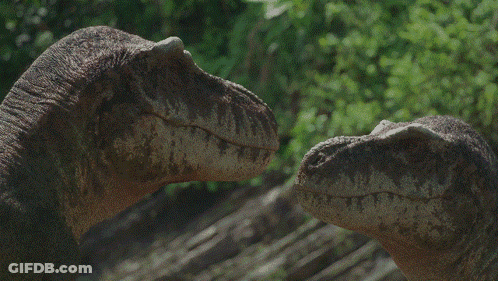 A Couple Of Dinosaurs Looking At Each Other With Trees Behind Them GIF