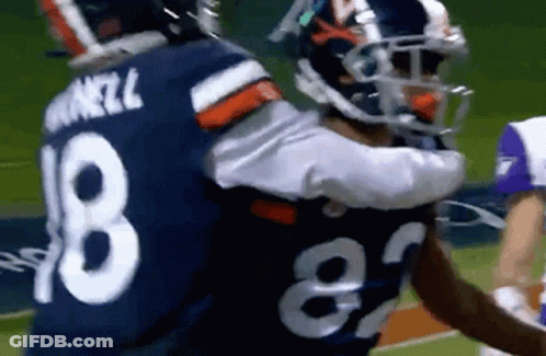 A Couple Of Football Players Hugging Each Other On The Field . GIF