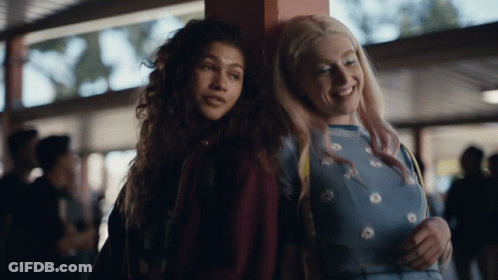 A Couple Of Girls Standing Next To Each Other And One Of Them Is Wearing A Blue Shirt With Daisies On It GIF