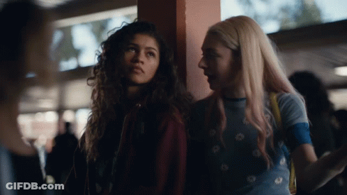 A Couple Of Girls Standing Next To Each Other With One Wearing A Blue Shirt With Daisies On It GIF
