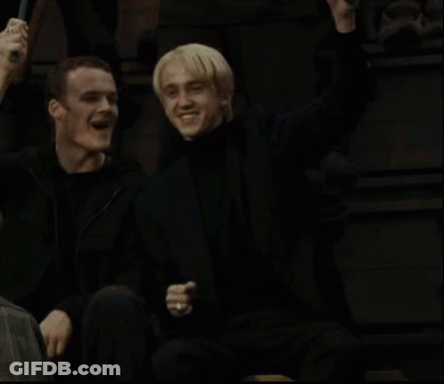 A Couple Of Men Are Sitting Next To Each Other In A Dark Room And Smiling . GIF