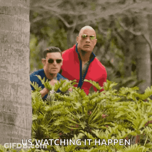A Couple Of Men Are Standing In The Woods And One Of Them Is Wearing Sunglasses And The Other Is Wearing A Red Jacket . GIF