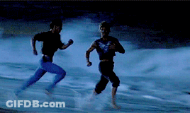 A Couple Of Men Running On A Beach At Night GIF