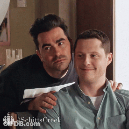 A Couple Of Men Sitting Next To Each Other With The Word Schitts Creek On The Bottom GIF