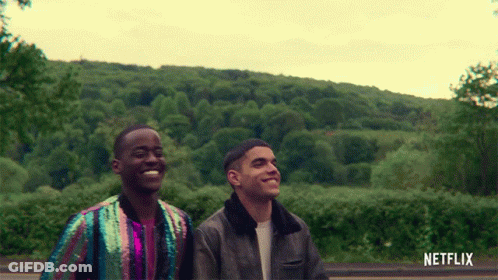 A Couple Of Men Standing Next To Each Other With A Netflix Logo Behind Them GIF