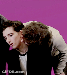 A Couple Of Men Standing Next To Each Other With A Pink Background GIF