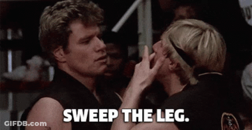 A Couple Of Men Standing Next To Each Other With The Words `` Sweep The Leg '' Written On The Bottom . GIF