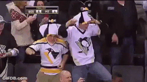 A Couple Of Men Wearing Penguin Jerseys Are Dancing In The Stands During A Hockey Game . GIF