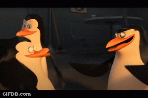 A Couple Of Penguins Standing Next To Each Other In A Dark Room GIF