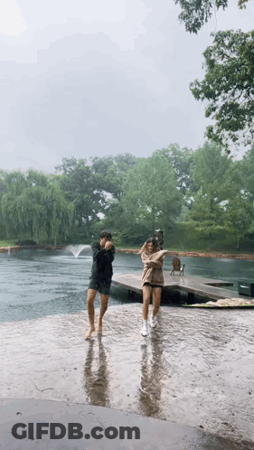 A Couple Of People Are Dancing In The Rain Near A Lake . GIF