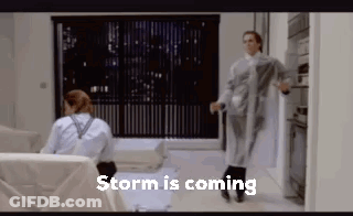 A Couple Of People Are Standing In A Living Room With The Words `` Storm Is Coming '' Written On The Bottom . GIF