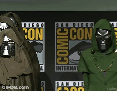A Couple Of People Are Standing In Front Of A Comic Con Sign GIF