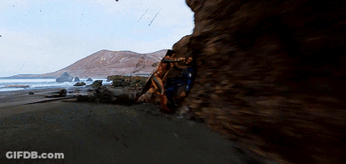 A Couple Of People Are Standing On A Rocky Beach GIF
