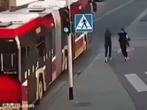 A Couple Of People Are Walking Down A Street Next To A Bus . GIF