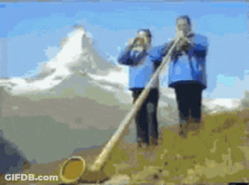 A Couple Of People Playing A Horn In Front Of A Mountain GIF