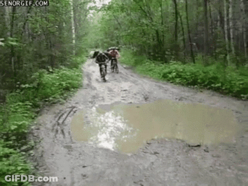 A Couple Of People Riding Bikes Down A Muddy Road . GIF