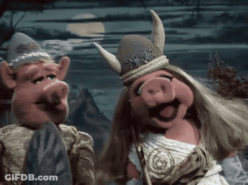 A Couple Of Pigs Standing Next To Each Other With One Wearing A Horned Hat GIF