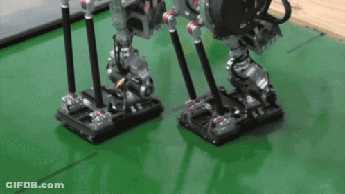 A Couple Of Robots Standing On A Green Surface GIF