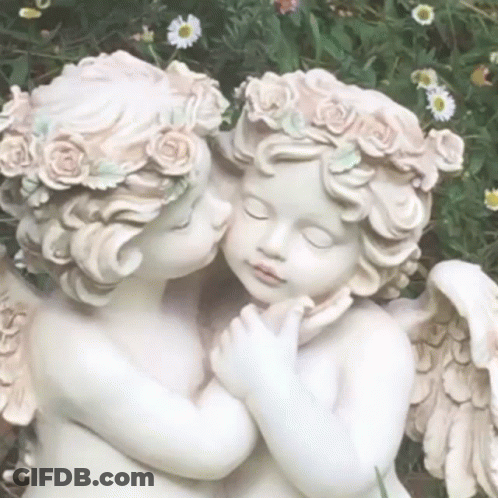 A Couple Of Statues Of Cherubs Kissing Each Other In A Garden . GIF