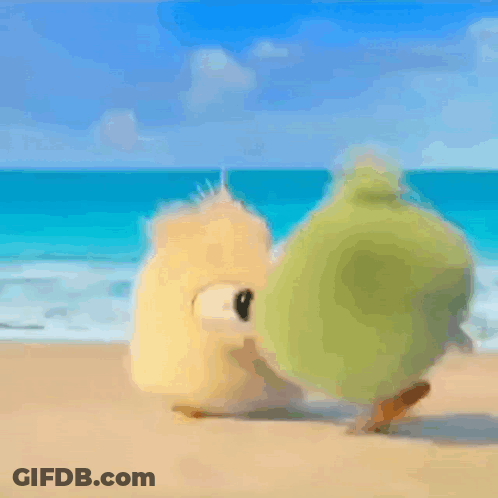 A Couple Of Stuffed Animals Are Standing On A Sandy Beach Near The Ocean . GIF