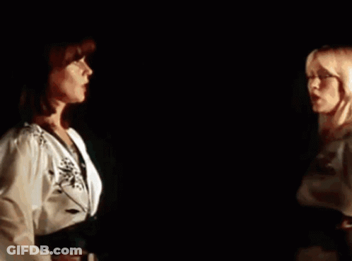 A Couple Of Women Are Standing Next To Each Other In A Dark Room . GIF