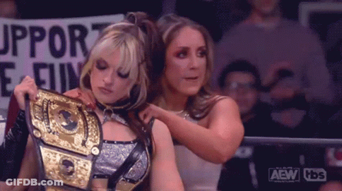 A Couple Of Women Are Standing Next To Each Other In A Ring Holding A Wrestling Championship Belt . GIF