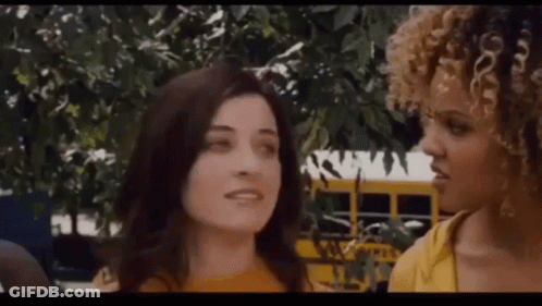 A Couple Of Women Are Standing Next To Each Other In Front Of A School Bus . GIF
