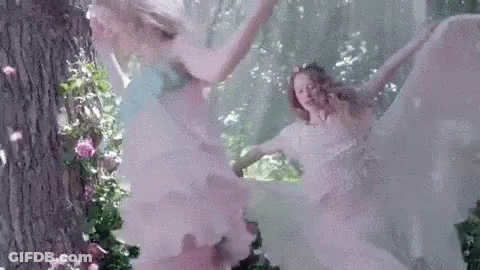 A Couple Of Women In White Dresses Are Dancing In The Woods . GIF