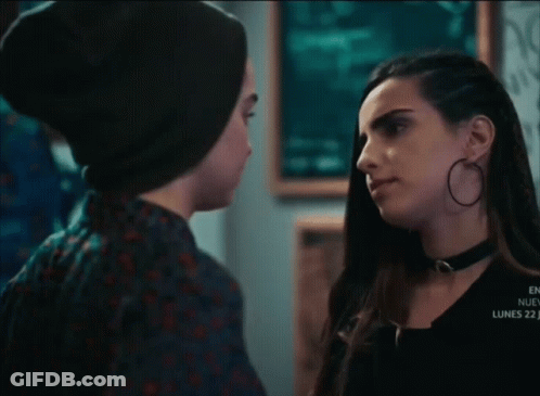 A Couple Of Women Looking At Each Other In A Dark Room With A Sign That Says Lucky 7 GIF