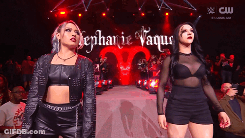 A Couple Of Women Standing On A Stage With The Name Stephanie Vaquer On The Screen GIF
