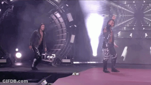 A Couple Of Wrestlers Are Walking On A Stage With A W Logo In The Corner GIF