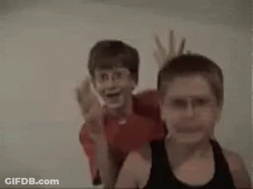 A Couple Of Young Boys Are Standing Next To Each Other . GIF