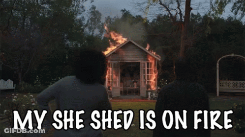 A Couple Standing In Front Of A Burning Shed With The Words My She Shed Is On Fire GIF