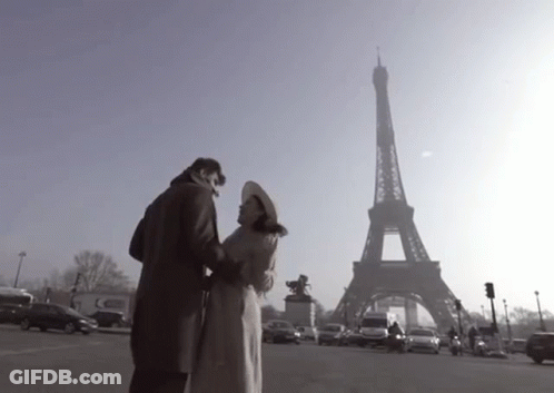 A Couple Standing In Front Of The Eiffel Tower In Paris GIF
