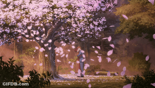 A Couple Standing Under A Tree With Petals Falling Around Them GIF
