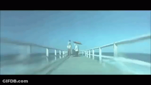 A Couple Walking On A Pier With Umbrellas GIF