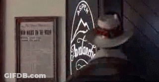 A Cowboy Hat Is Sitting On A Table Next To A Framed Newspaper And A Sign . GIF
