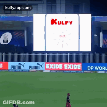 A Cricket Game Is Being Played In Front Of A Large Screen That Says Kulfy Out GIF
