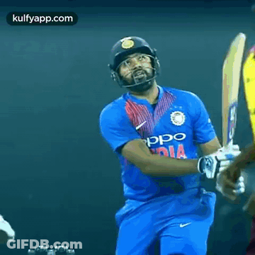 A Cricket Player In A Blue Jersey With The Word India On It Is Standing In Front Of Another Player . GIF