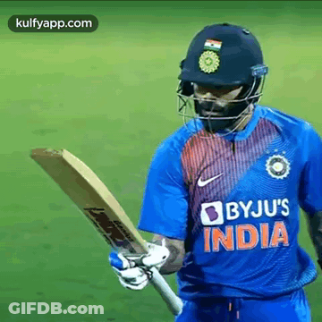 A Cricket Player Is Wearing A Helmet And Holding A Bat On A Field . GIF