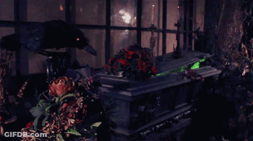 A Crow Sits On Top Of A Coffin With A Green Light On It GIF