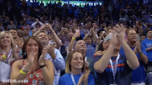 A Crowd Of People Are Applauding In Front Of A Sign That Says Team Partners GIF