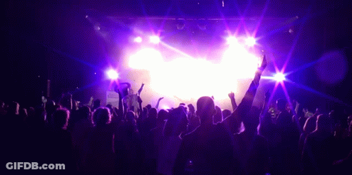 A Crowd Of People Are Dancing In Front Of A Stage With Purple Lights GIF