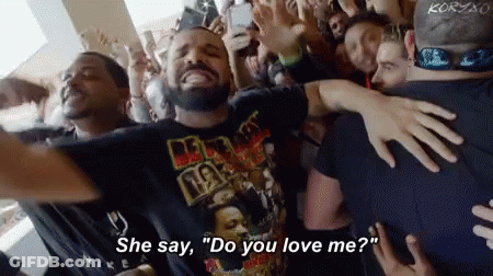 A Crowd Of People Are Gathered Around A Man Wearing A T-Shirt That Says " Do You Love Me " GIF