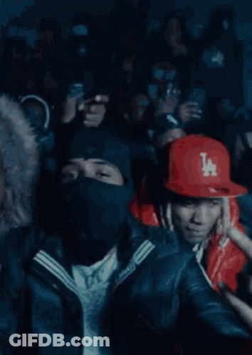 A Crowd Of People Are Gathered In A Dark Room And One Man Is Wearing A Red Jacket With A Ny Logo On It GIF