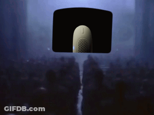 A Crowd Of People Are Gathered In A Dark Room With A Microphone Hanging From The Ceiling GIF