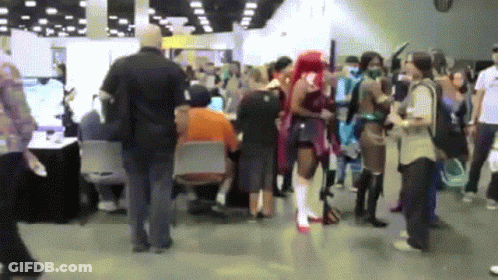 A Crowd Of People Are Gathered In A Room With A Man In An Orange Shirt Sitting At A Table GIF